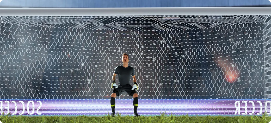 Un gardien de but, vêtu de noir et concentré, se tient devant ses cages, prêt à défendre. Le stade est plein à craquer, les projecteurs brillent, créant une ambiance électrique.
